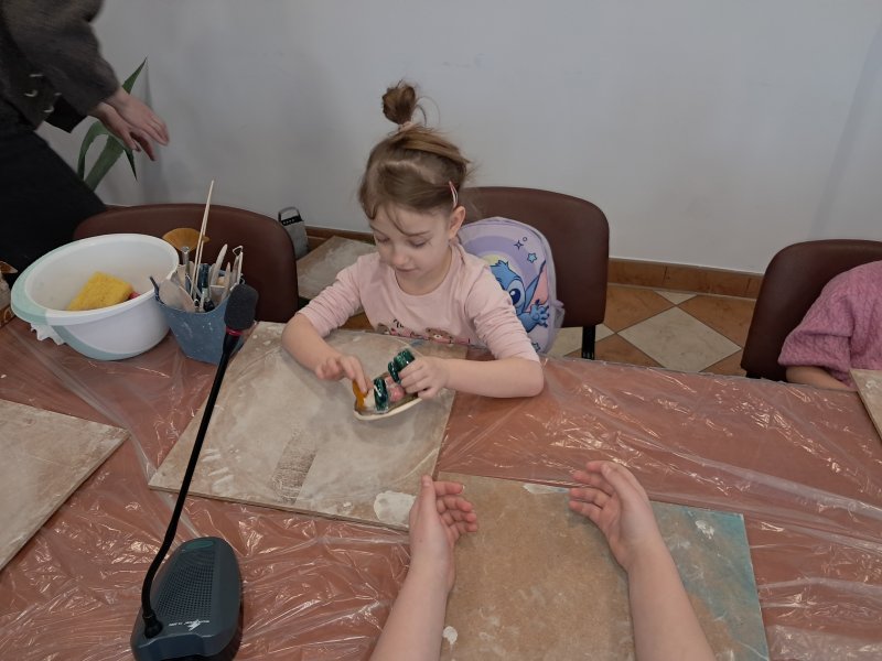 Zdjęcie przedstawia uczestniczkę zajęć z ceramiki siedzącą na krześle przy stoliku w trakcie zajęć  