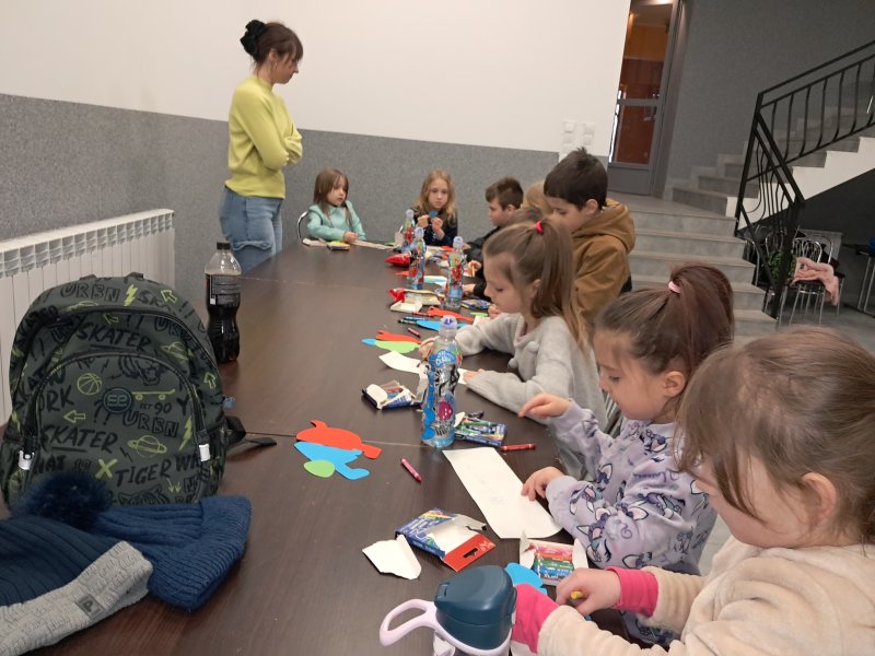 Zdjęcie przedstawia uczestników zajęć siedzących na krzesłach przy stoliku w trakcie zajęć plastycznych  