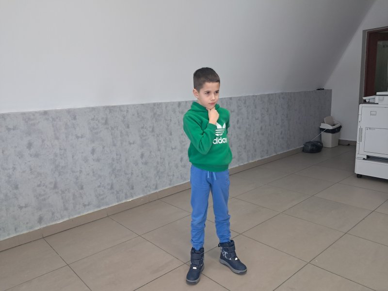 Na zdjęciu widać stojącego chłopca w trakcie gry w kalambury w sali, w której odbywały się zajęcia.  