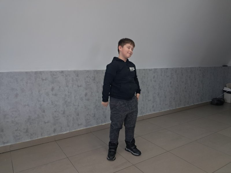 Na zdjęciu widać stojącego chłopca w trakcie gry w kalambury w sali, w której odbywały się zajęcia.  