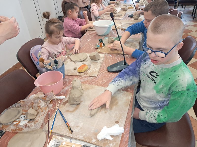 Zdjęcie przedstawia uczestników zajęć siedzących na krzesłach przy stoliku w trakcie warsztatów z ceramiki  