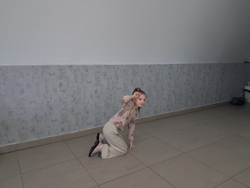 Na zdjęciu widać  wspierającą się na rękach na podłodze dziewczynkę w trakcie gry w kalambury w sali, w której odbywały się zajęcia.  