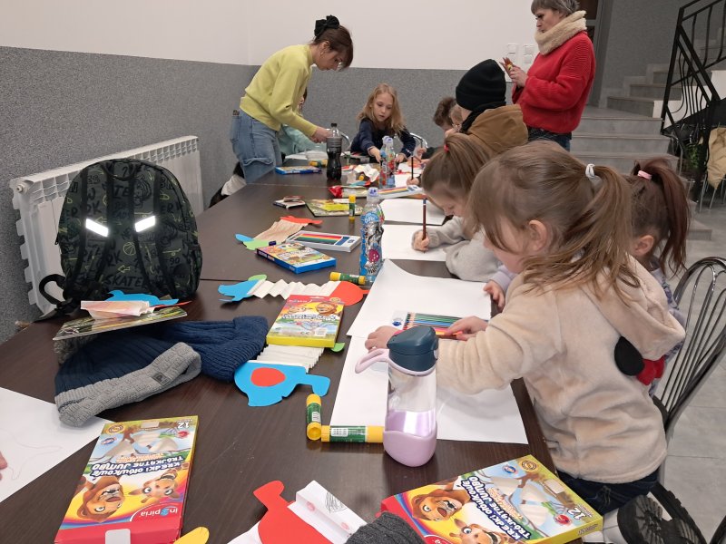 Zdjęcie przedstawia uczestników zajęć siedzących na krzesłach przy stoliku w trakcie zajęć plastycznych  