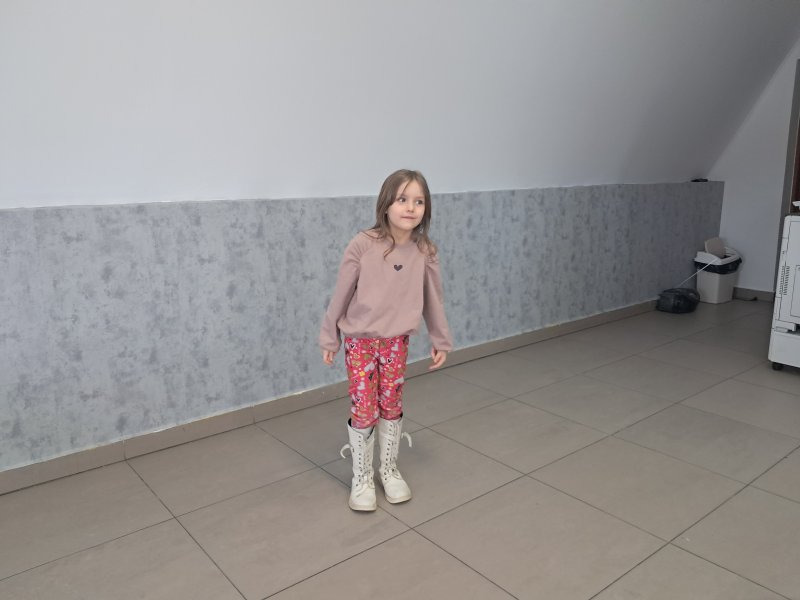 Na zdjęciu widać stojącą dziewczynkę w trakcie gry w kalambury w sali, w której odbywały się zajęcia.  