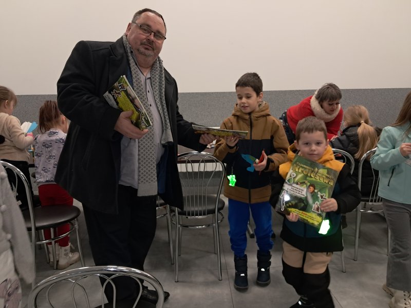 Zdjęcie przedstawi dyrektora biblioteki wręczającego dzieciom stojącym obok niego książeczki  