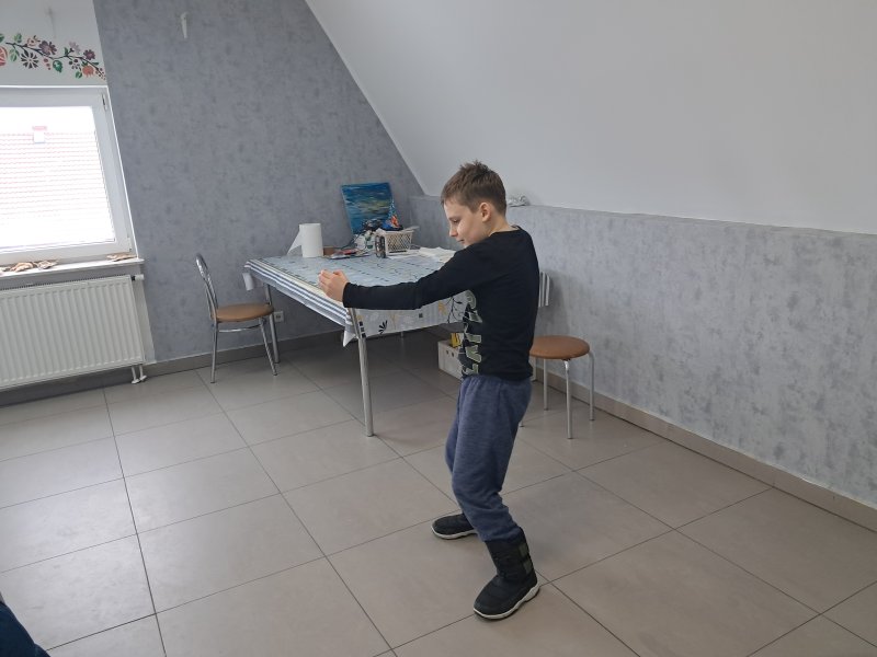 Na zdjęciu widać chłopca gestykulującego rękami w trakcie gry w kalambury w sali, w której odbywały się zajęcia.  