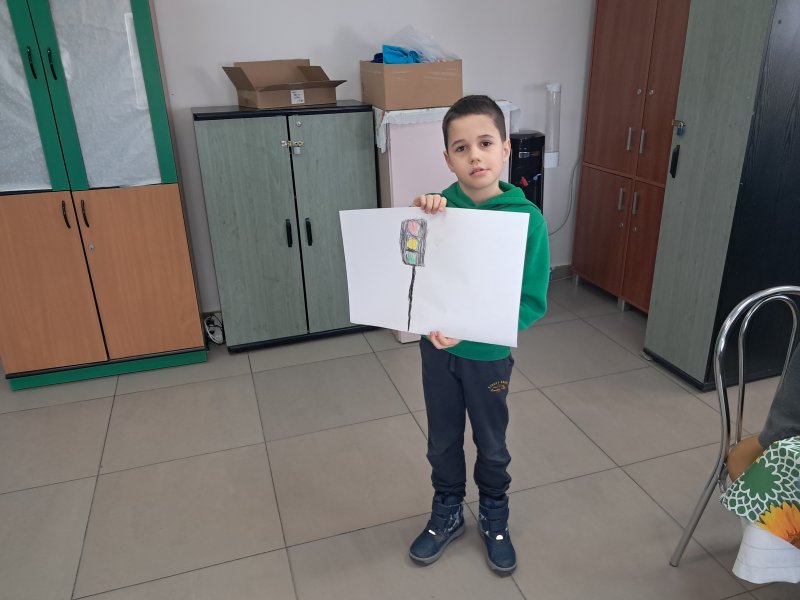 Zdjęcie przedstawia chłopca stojącego i pozującego do zdjęcia z własnym rysunkiem  