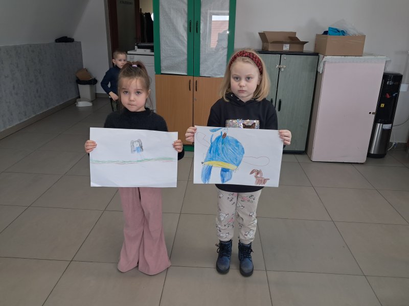 Zdjęcie przedstawia dziewczynki stojące i pozujące do zdjęcia z własnym rysunkiem  