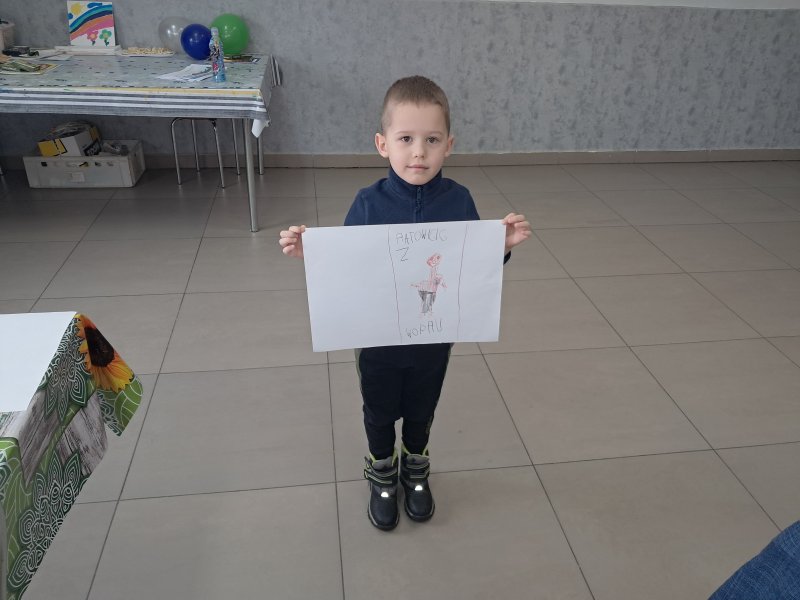 Zdjęcie przedstawia chłopca stojącego i pozującego do zdjęcia z własnym rysunkiem  