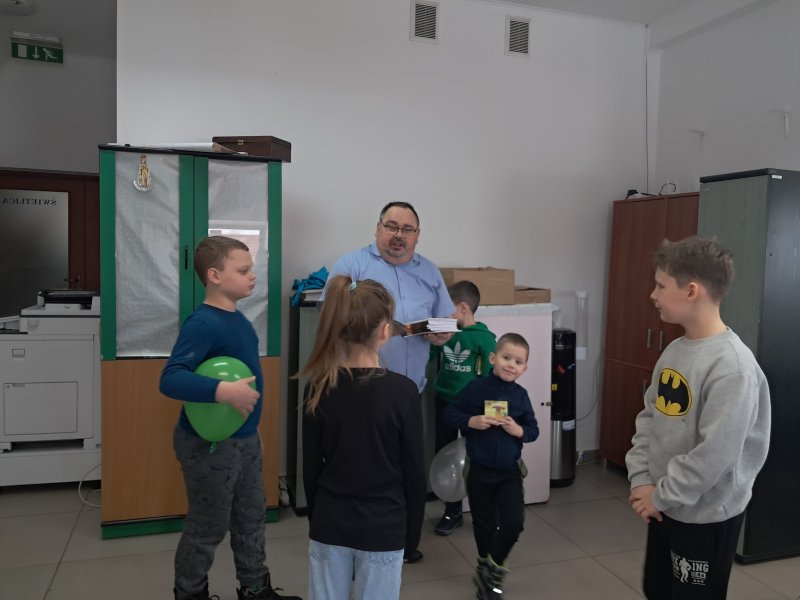 Zdjęcie przedstawia dyrektora biblioteki wręczającego dzieciom książeczki  