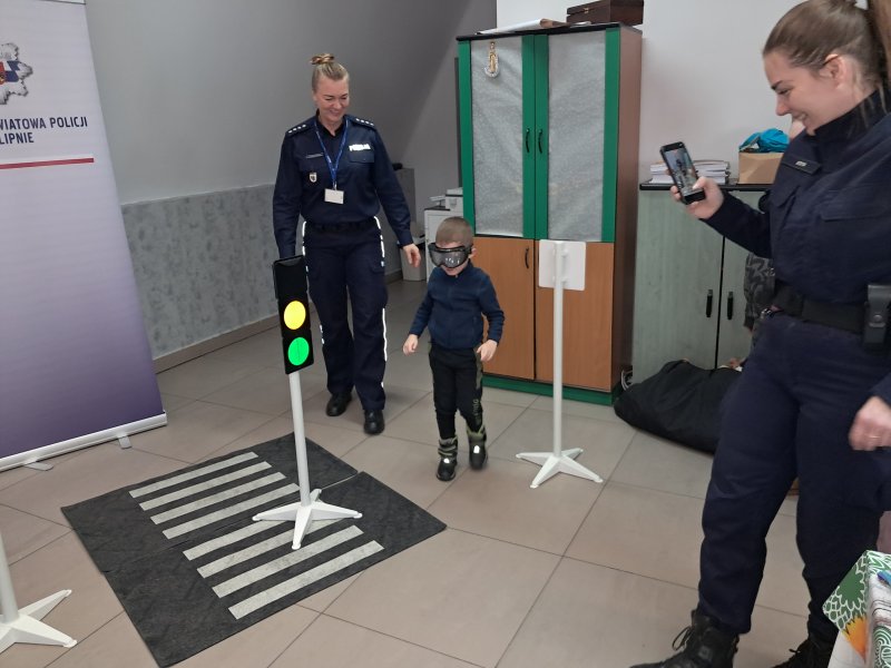 Zdjęcie przedstawia rzecznika prasowego policji Małgorzatę Małkińską i uczestniczkę zajęć w trakcie scenki sytuacyjnej z alkogoglami na zainscenizowanym przejściu dla pieszych w sali, w której odbywały się zajęcia.  