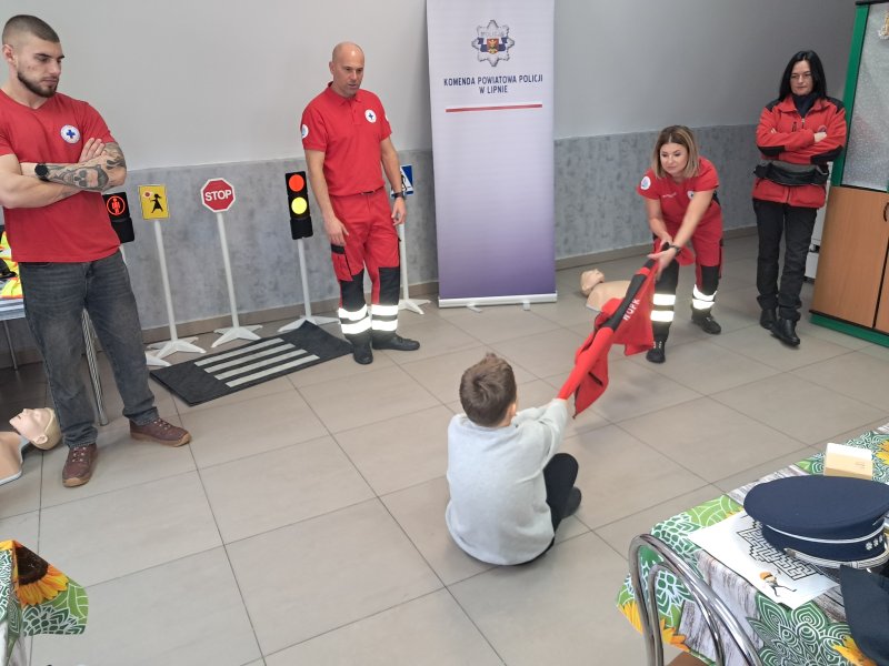 Zdjęcie przedstawia scenkę w sali z udziałem uczestnika zajęć z wykorzystaniem odzieży przez ratownika do nauki wyciągania z wody tonącej osoby.  