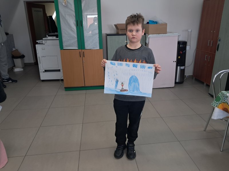 Zdjęcie przedstawia dziewczynkę stojącą i pozującą do zdjęcia z własnym rysunkiem  