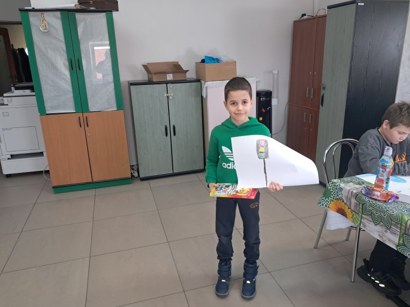 Zdjęcie przedstawia chłopca stojącego i pozującego do zdjęcia z własnym rysunkiem  