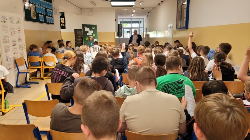 Zdjęcie przedstawia widok ogólny na uczestników spotkania przed którymi stoi dyrektor biblioteki  
