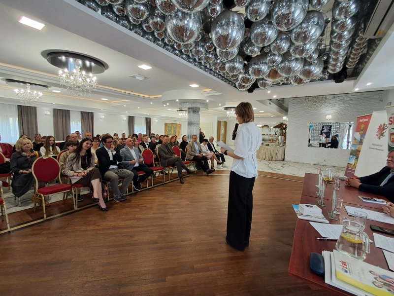 Zdjęcie przedstawia laureatkę konkursu stojącą przed uczestnikami konkursu i czytającą nagrodzony wiersz.   