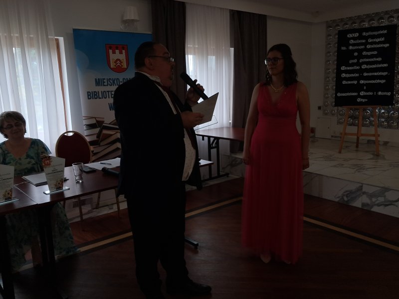 Zdjęcie przedstawia dyrektora biblioteki wręczającego podziękowanie za występ artystyczny w trakcie gali konkursowej Martynie Kumor  