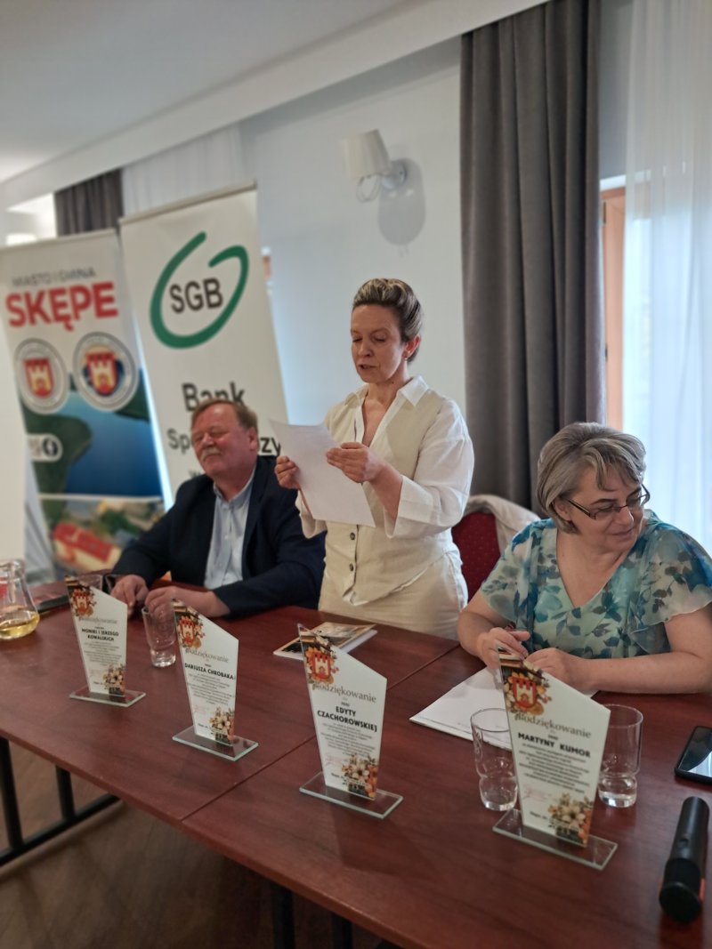 Zdjęcie przedstawia stolik jurorów w momencie czytania przez jurorkę wiersza laureata konkursu  