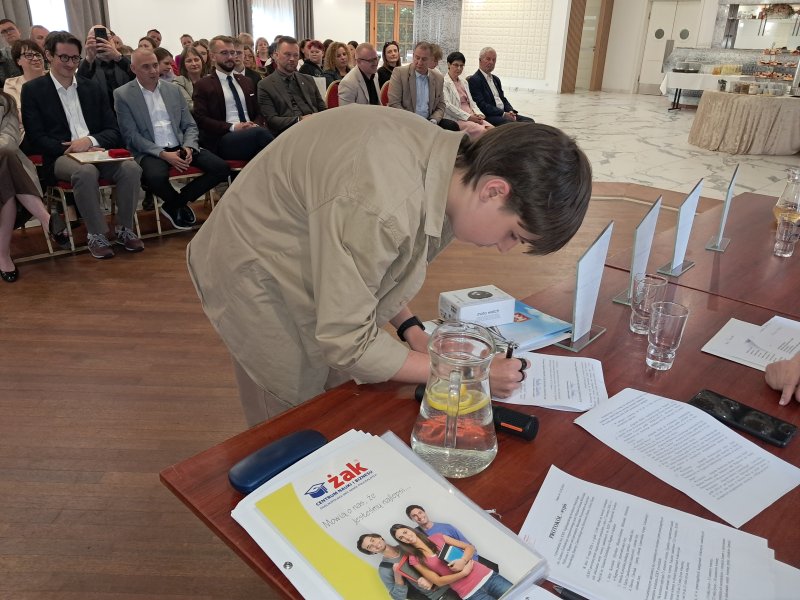 Zdjęcie przedstawia laureata konkursu kwitującego na liście odbiór nagrody  