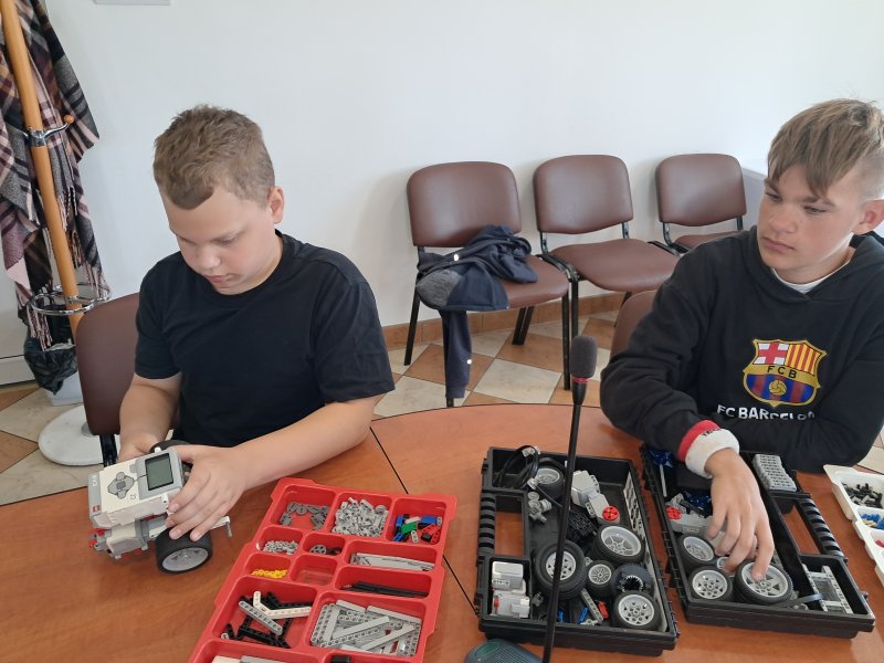 Zdjęcie przedstawia uczestników zajęć  układających klocki Lego w trakcie zajęć z robotyki w sali urzędu   