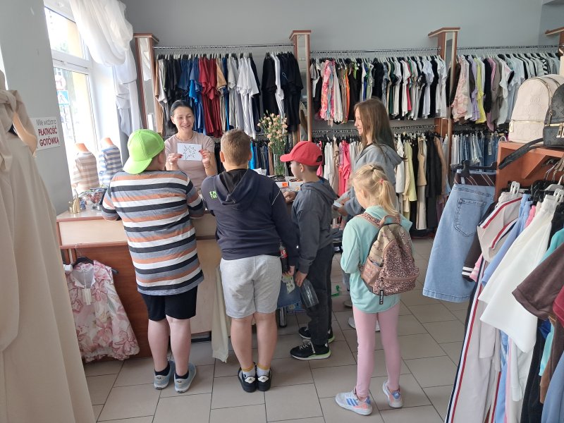 Zdjęcie przedstawia uczestników gry miejskiej odczytujących zadanie z koperty w sklepie odzieżowym  