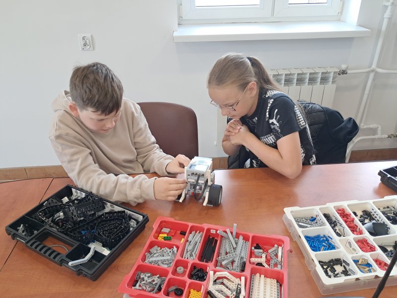 Zdjęcie przedstawia uczestników zajęć  układających klocki Lego w trakcie zajęć z robotyki w sali urzędu   