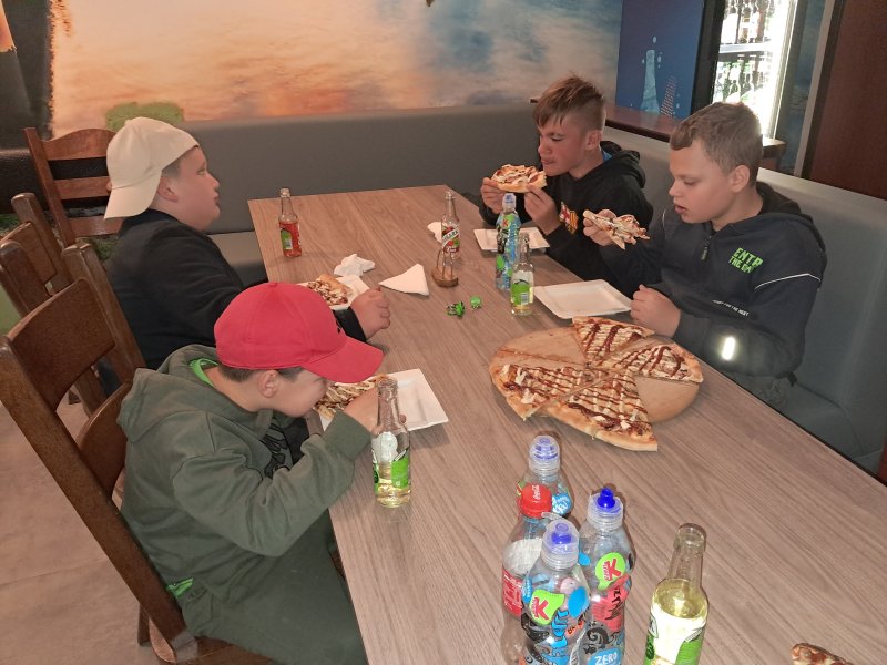 Zdjęcie przedstawia dzieci siedzące przy stoliku w barze jedzące pizzę.  