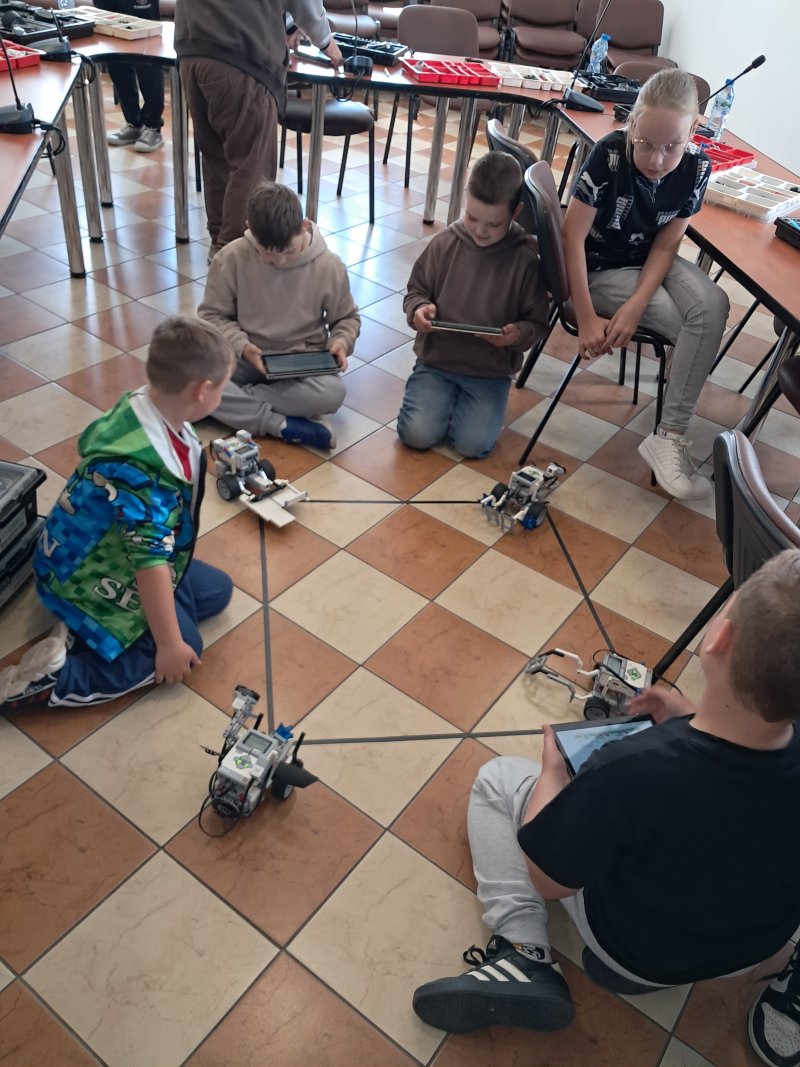 Zdjęcie przedstawia dzieci siedzące na podłodze bawiące się robotami z klocków Lego  
