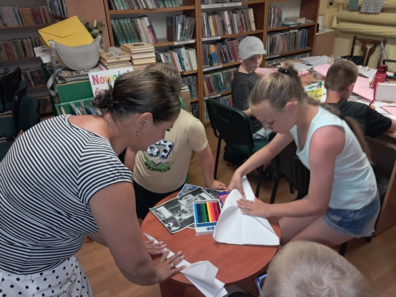 Zdjęcie przedstawia uczestników zajęć plastycznych w trakcie składania samolotu z kartki papieru   