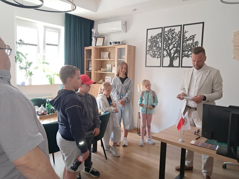Zdjęcie przedstawia uczestników gry miejskiej w gabinecie Burmistrza Skępego. Burmistrz odczytuje uczestnikom pierwsze zadanie rozpoczynające grę miejską.  