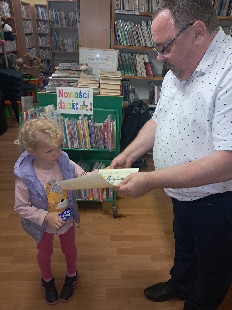 Dyrektor biblioteki w Skępem wręcza Dyplom Małego Czytelnika dziewczynce w bibliotece  